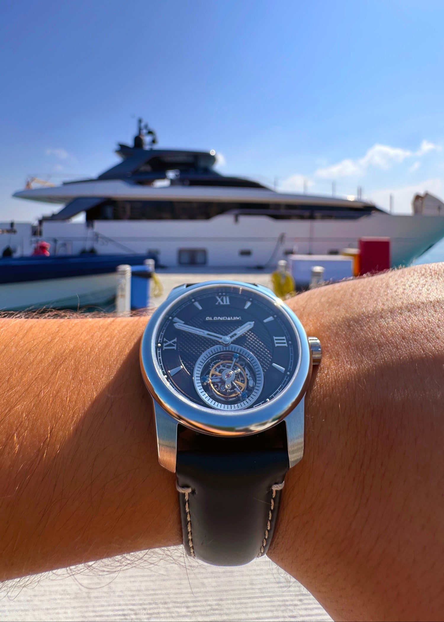 Wrist wearing a watch with a large yacht in the background
