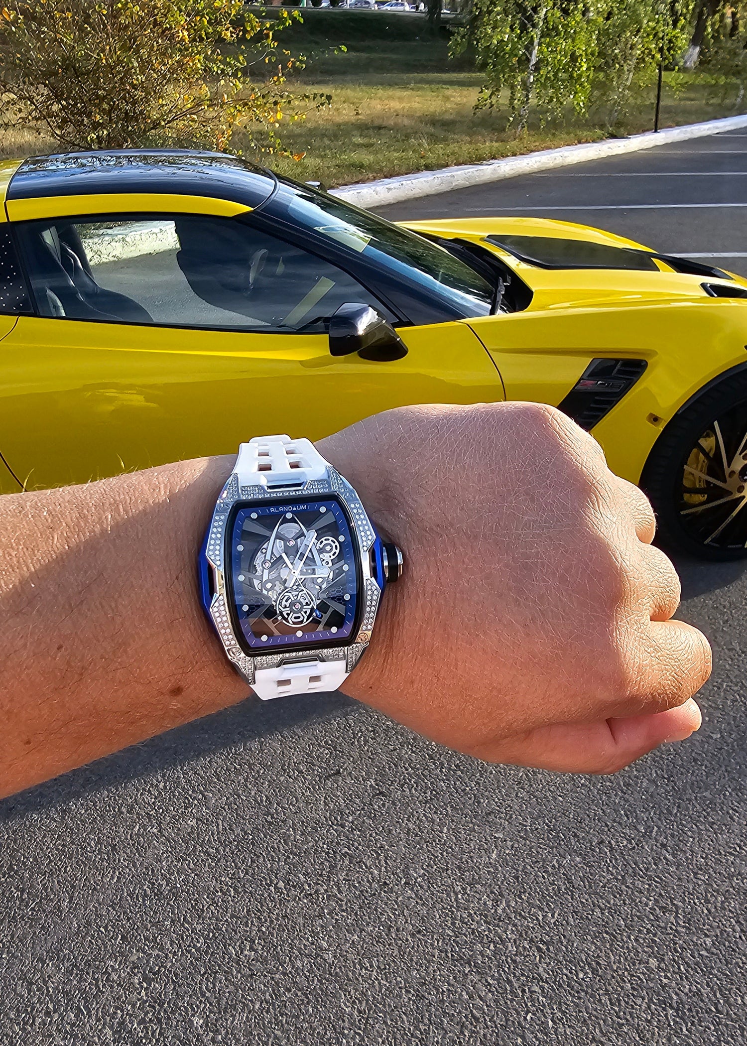 Hand wearing a luxury watch with a yellow car in the background