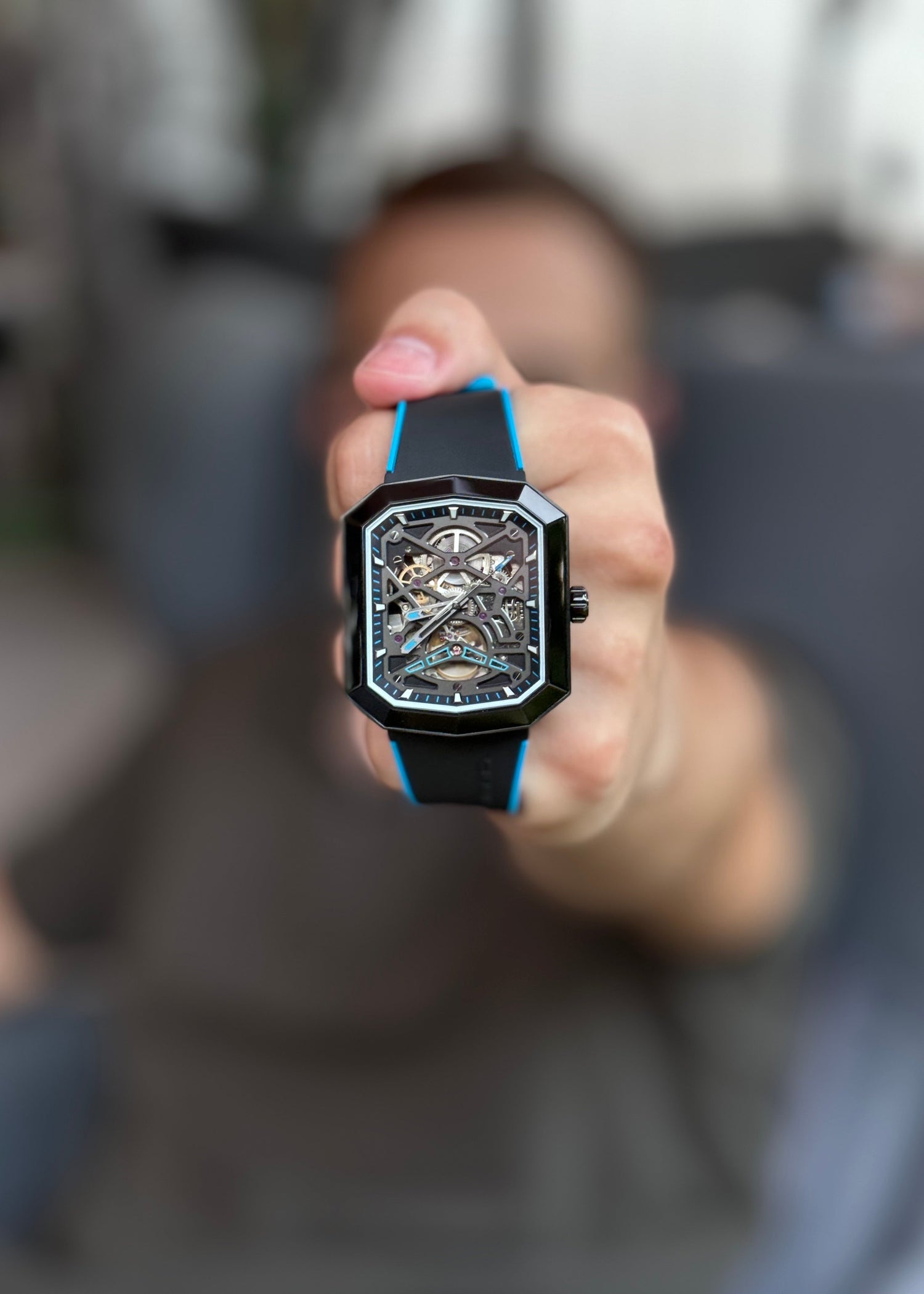 Hand holding a black wristwatch with a blurred background