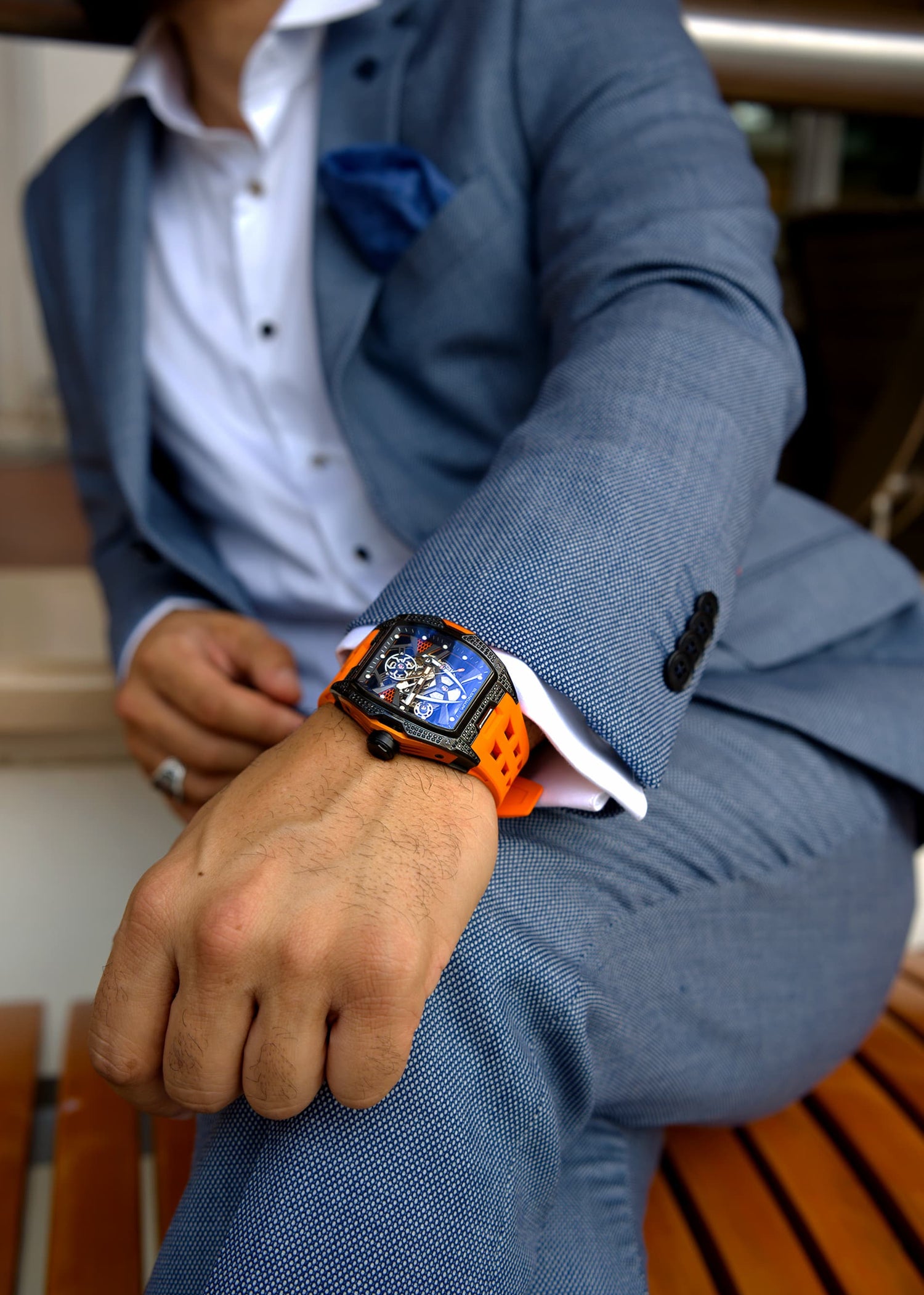 Person wearing a blue suit with a colorful smartwatch on a wooden bench.
