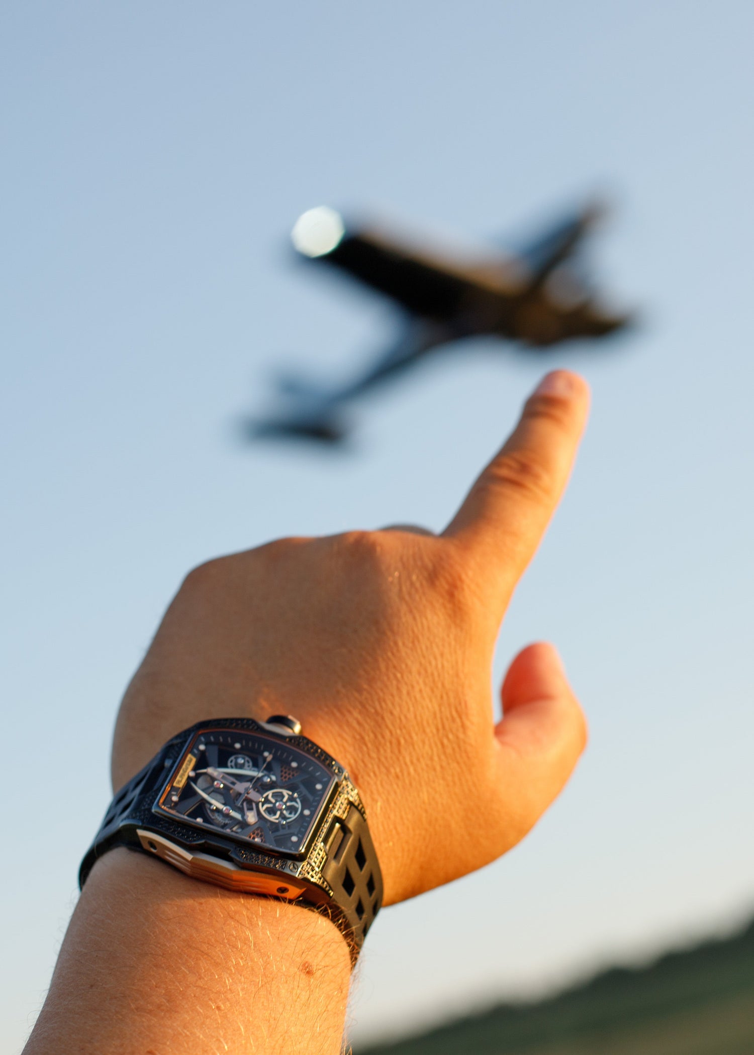 Hand pointing at an airplane in the sky with a clear blue background