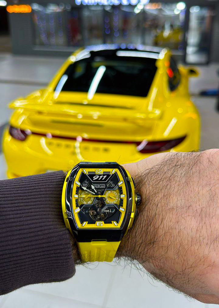 Person wearing a yellow and black watch with a car in the background